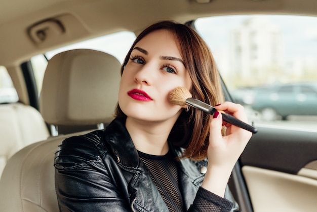 Young girl retouching her makeup while stopped in the traffic Free Photo