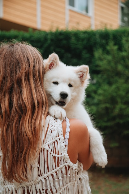 サモエド犬の子犬を手に持って外に立っている若い女の子 ペットのコンセプトを持っています かわいい動物のコンセプトです プレミアム写真