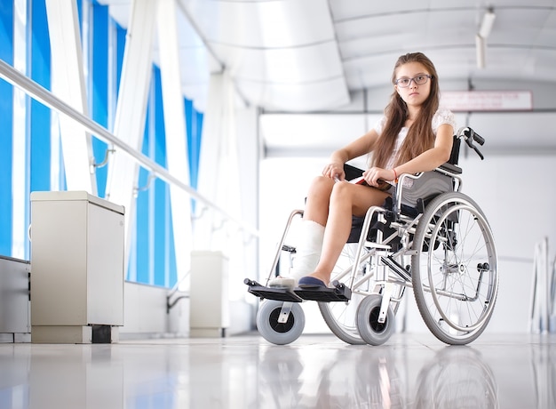 A young girl in a wheelchair is reading a book, patient in a wheelchair in the hospital corridor. Premium Photo