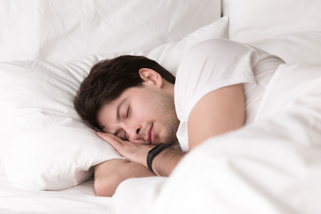 Young guy sleeping in bed wearing smartwatch or sleep tracker Free Photo