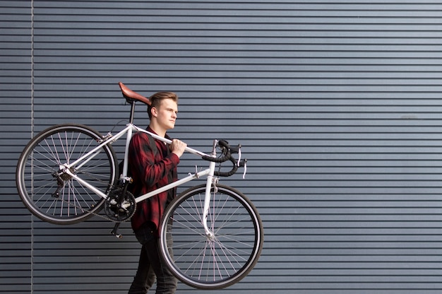 若いハンサムな男が壁に彼の肩に壊れた自転車を運ぶ プレミアム写真