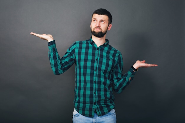 評価の質問 緑の市松模様のシャツ 灰色の背景を手を繋いでいる若いハンサムな流行に敏感なひげを生やした男 無料の写真