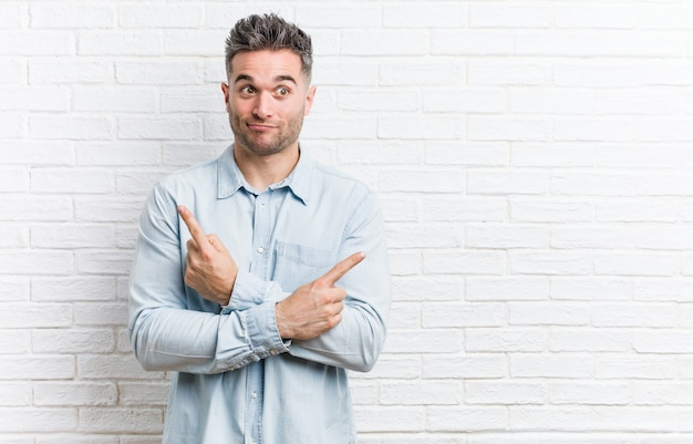 Young handsome man against a bricks wall points sideways, is trying to choose between two options. Premium Photo