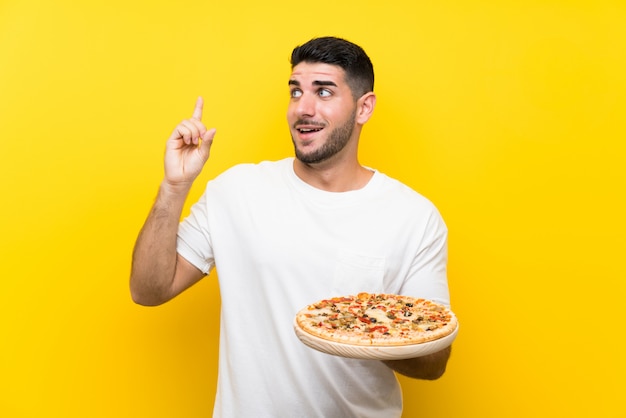 Premium Photo | Young handsome man holding a pizza over isolated yellow ...