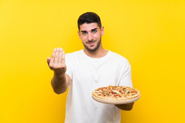 Premium Photo | Young handsome man holding a pizza over isolated yellow ...