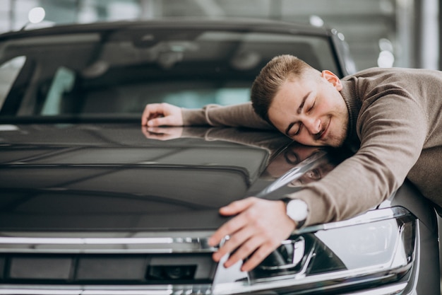 Young handsome man hugging a car in a car showroom Free Photo