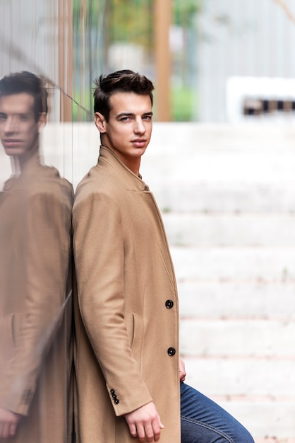 Premium Photo | Young handsome man with coat leaning on a reflective ...
