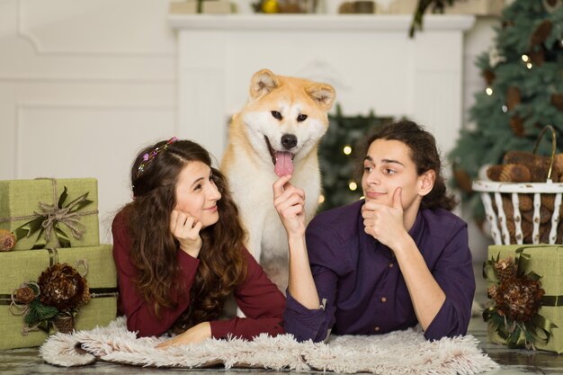 自宅でクリスマス休暇の床に愛らしい秋田犬犬を抱きしめる若い幸せなカップル プレミアム写真