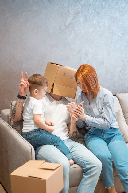 ソファの上に座って一緒に箱を開ける子供と若い幸せな家族 無料の写真