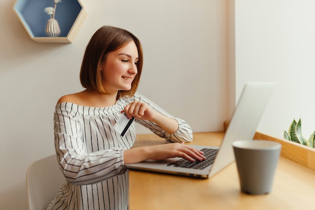 Young happy female holding credit card and using laptop computer.  Free Photo