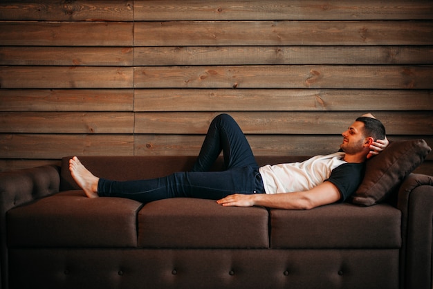 Молодой счастливый человек, лежа на диване, вид сбоку. отдых на диване.  человек мужского пола расслабиться | Премиум Фото