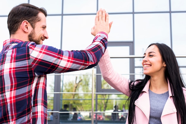 Free Photo | Young happy man and woman friends giving high five near glass building