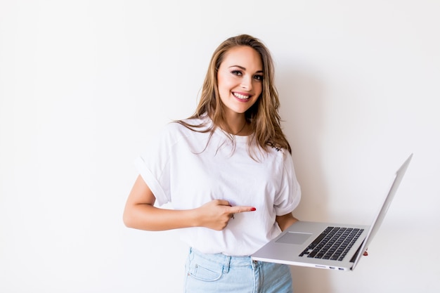 Молодая счастливая улыбающаяся женщина в повседневной одежде держит ноутбук и отправляет электронное письмо своему лучшему другу Бесплатные Фотографии