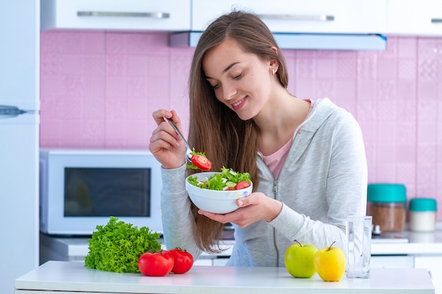 Premium Photo | Young healthy woman in sportswear eating fresh vegetable  salad at home in kitchen. balanced organic diet and clean fitness eating.