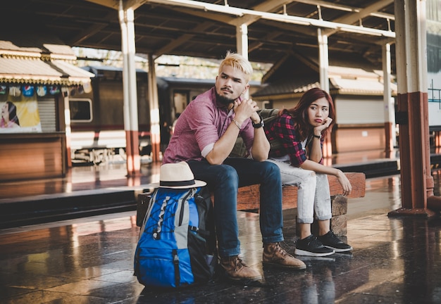 Young hipster couple sitting on wooden bench at train station. Couple ...