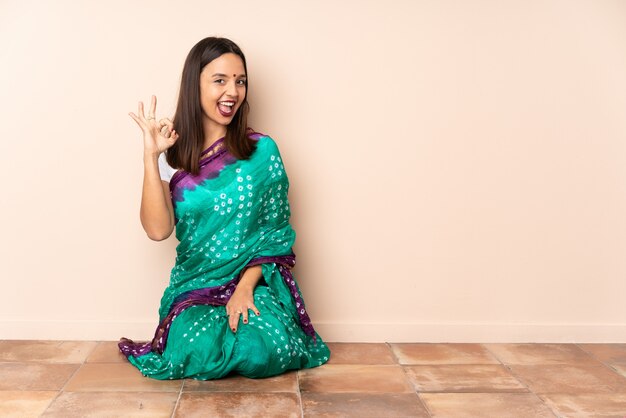 指でokの標識を示す床に座っている若いインド人女性 プレミアム写真