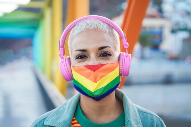 レインボーフラッグマスクを着用しながらヘッドフォンで音楽を聴く若いレズビアン プレミアム写真
