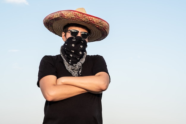 若い男性は 伝統的なソンブレロ バンダナでギャングに扮した 盗賊や西洋スタイルの盗賊を装った男のメキシコのお祭りやハロウィーンのコンセプト プレミアム写真