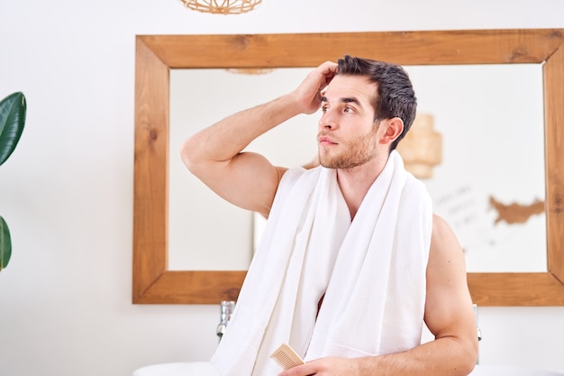 Premium Photo | Young male stroking his hair while standing by mirror