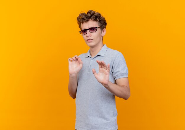 Free Photo Young Man In Black Glasses Wearing Grey Polo Shirt Making Stop Sign Holding Hands Out As Telling Do Not Come Closer Scared Standing Over Orange Wall