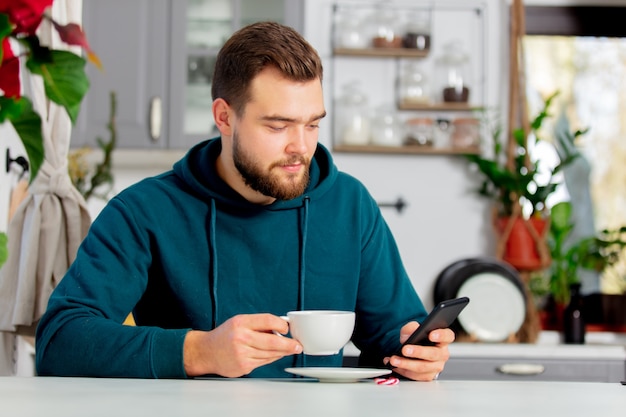 Young man drinks coffee and uses a mobile phone Premium Photo