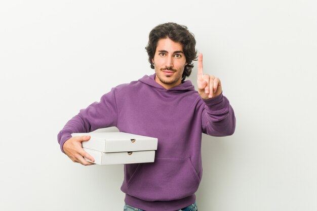 Young man holding pizzas package showing number one with finger. Premium Photo