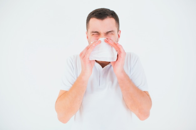 Young man isolated over white wall. cover nose with white tissue. sick and ill person sneezing