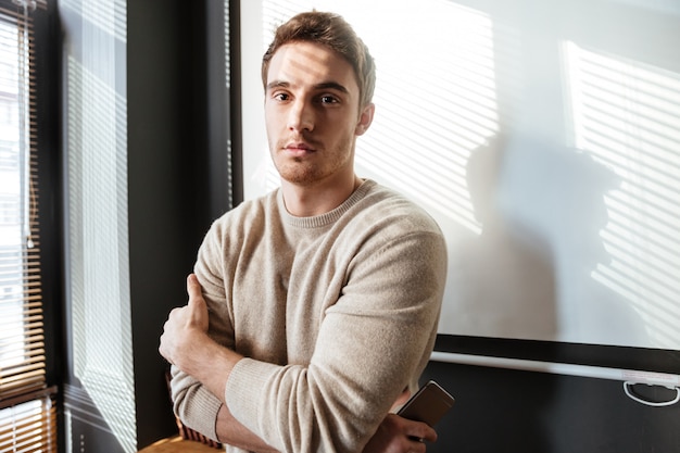 Free Photo Young Man In Office Looking At Camera While Holding Phone