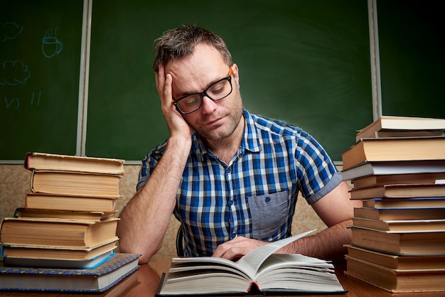 Premium Photo | A young man reads a book at a table with stacks of books.