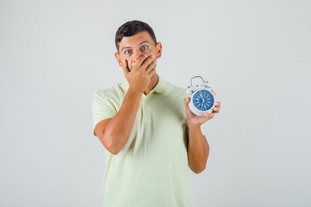 Free Photo | Young man in t-shirt covering mouth and holding alarm ...