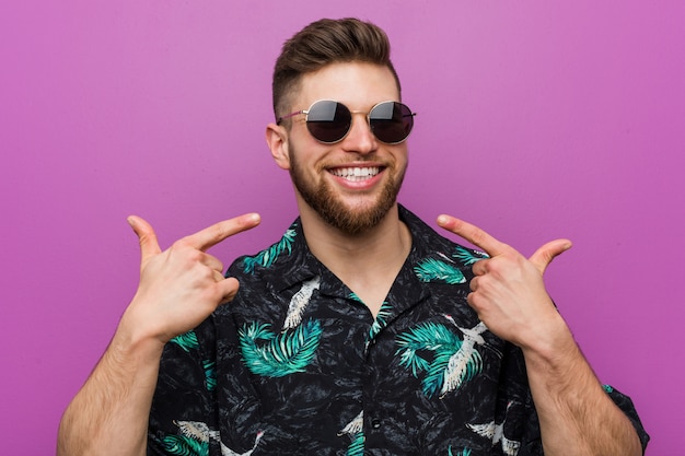 Young man wearing a vacation look smiles, pointing fingers at mouth. Premium Photo