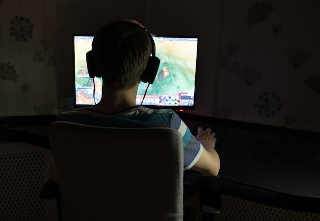 暗い部屋でコンピューターゲームをプレイするヘッドフォンと若い男 プレミアム写真