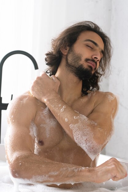 お湯と泡でお風呂を楽しみながら目を閉じて体を洗う若い筋肉男 プレミアム写真