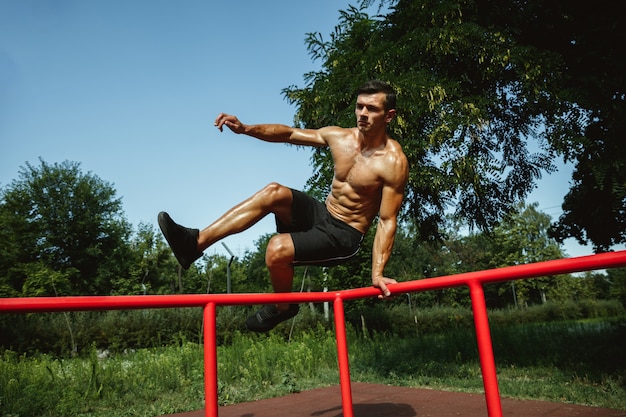 晴れた夏の日に遊び場で鉄棒の上にジャンプする若い筋肉の上半身裸の白人男性 彼の上半身を屋外でトレーニングします スポーツ トレーニング 健康的なライフスタイル 幸福の概念 無料の写真