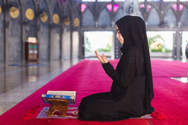Young muslim woman in wear black dress read quran and making wish praying in mosque. make a wish and read quran in ramadan. Premium Photo