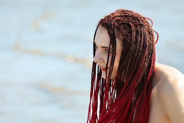 緋色のドレッドヘアを持つ若い裸の女性は海のそばで自然を楽しんでいます プレミアム写真