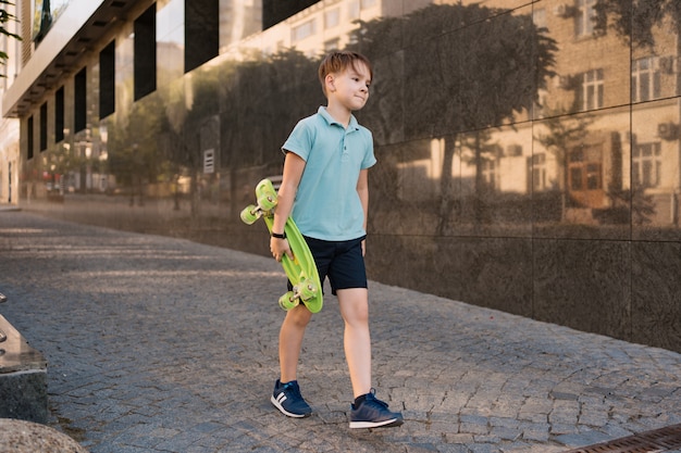 無料の写真 ペニーボードを手に歩いて明るい服を着た若い学校のクールな男の子