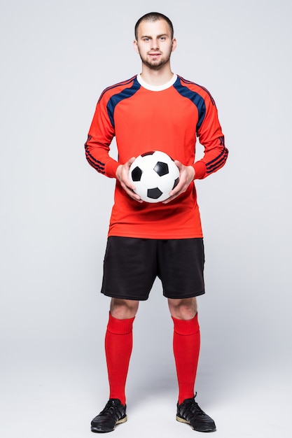 白の前に赤いジャージに身を包んだボールを持つ若いサッカー選手 無料の写真