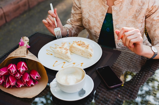 カフェに座っている カプチーノのカップを保持している おいしいケーキを食べる若いスタイリッシュな女性 無料の写真