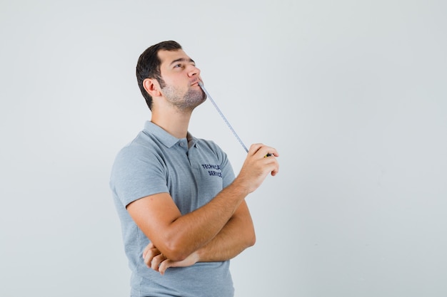 Free Photo Young Technician In Grey Uniform Holding Tape Measure In One Hand And Standing In Thinking Pose And Looking Pensive