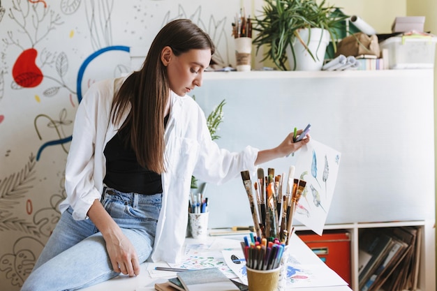 Premium Photo | Young thoughtful painter leaning on desk holding paper ...