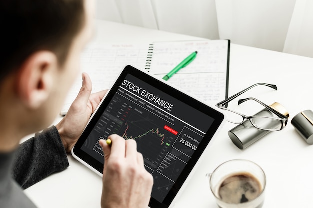 Young trader is sitting in home at table, working on tablet with graphs Premium Photo
