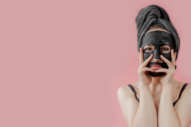 Premium Photo | Young woman apply black cosmetic fabric facial mask on pink  background. face peeling mask with charcoal, spa beauty treatment, skincare,  cosmetology. close up
