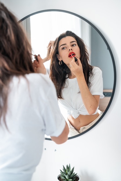 Young woman applying lipstick looking at mirror Free Photo