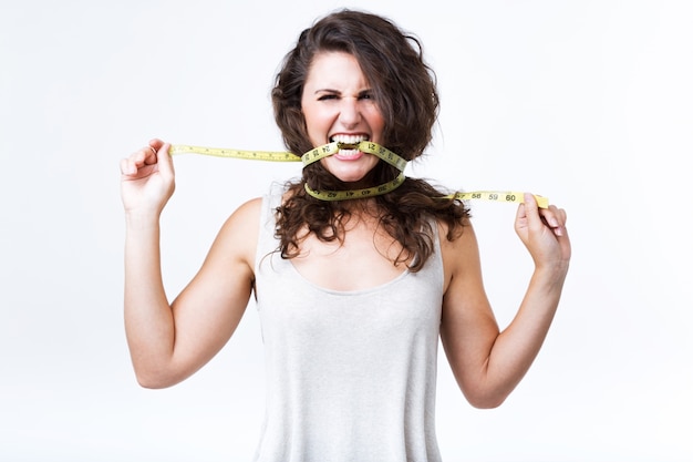 Young woman biting tape measure over white background. Free Photo