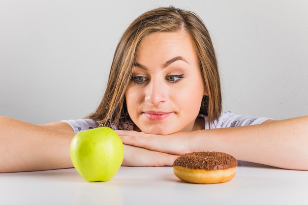 Young woman choosing to eat apple instead of donut Free Photo