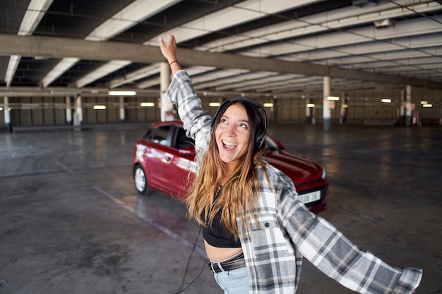 駐車場で彼女の車の前で踊ったりジャンプしたりする若い女性 彼女は幸せで頭がおかしい プレミアム写真