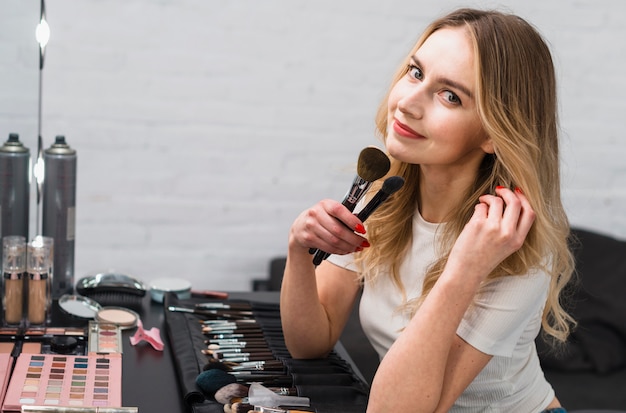 Free Photo | Young woman holding makeup brushes sitting in studio