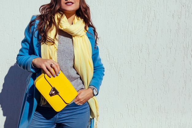 Young woman holding stylish yellow handbag and wearing trendy blue coat. spring female clothes and accessories. fashion. color of 2021 Premium Photo