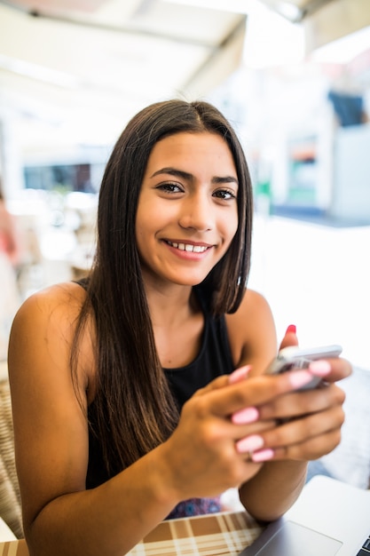 彼女の電話からテキストメッセージを読んでカフェの若い女性 ノートパソコンとスマートフォンを使用してカフェのテーブルに座っているラテン系の女性 無料の写真